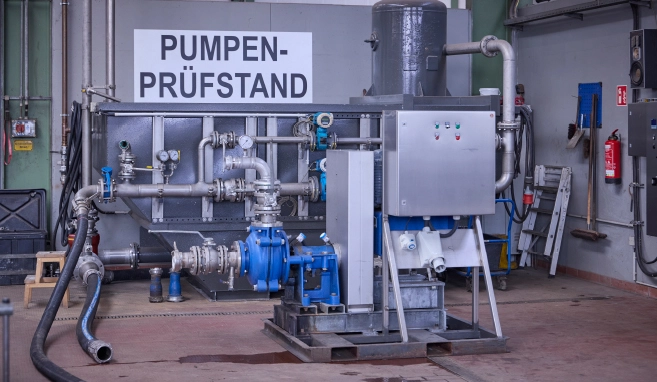 Pumpenprüfstand mit Rohrleitungen, Ventilen und Messinstrumenten in einer Industriehalle.