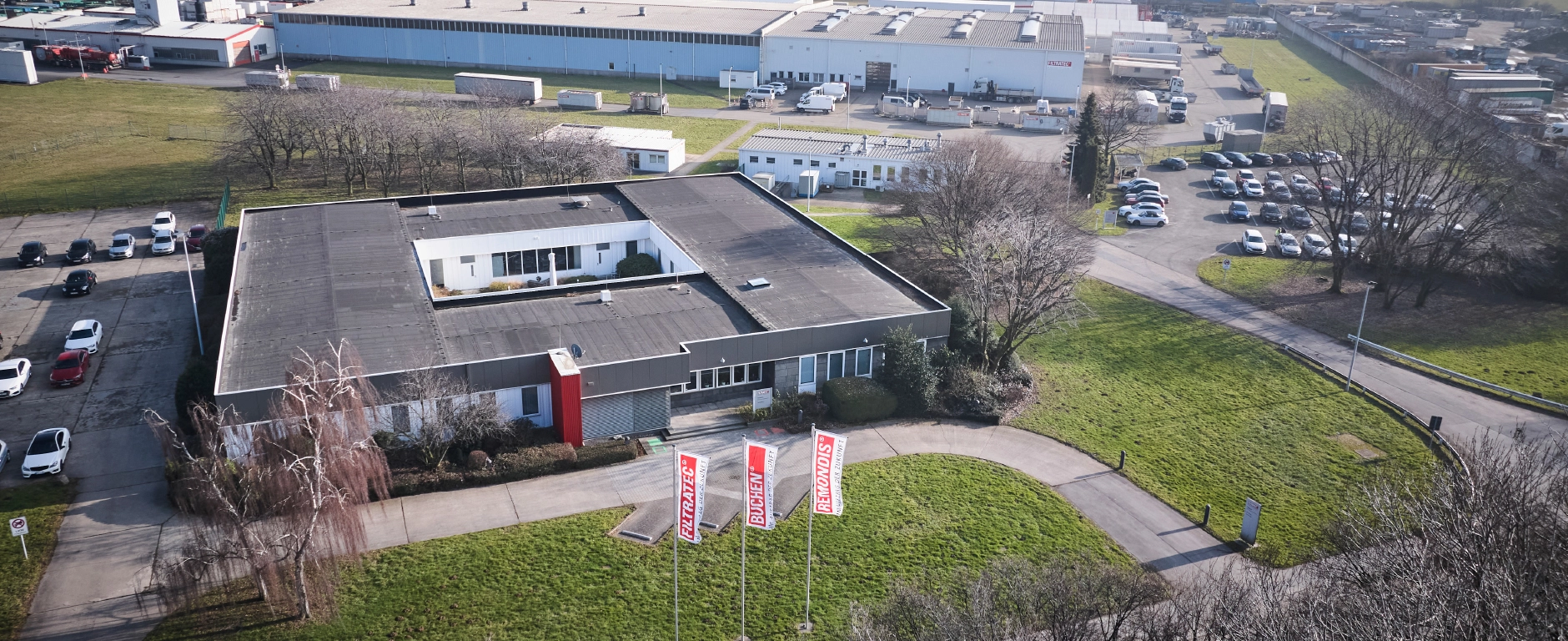 Luftaufnahme eines Unternehmensgeländes mit Bürogebäude, Produktionshallen und Fahnen von FILTRATEC, BUCHEN und REMONDIS.