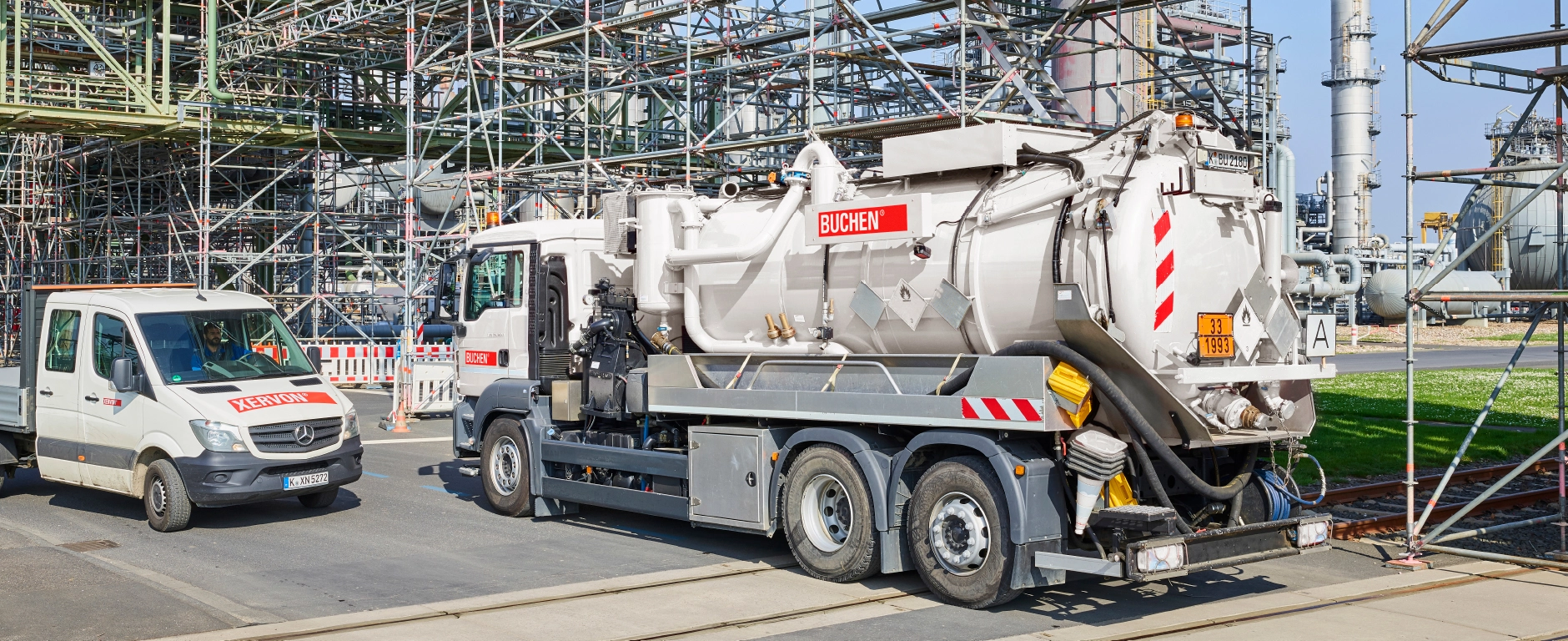Industrieanlage mit Rohrleitungen und Gerüstkonstruktion, davor ein Saugfahrzeug von BUCHEN und ein Servicefahrzeug auf dem Betriebsgelände.