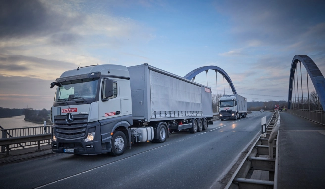 Zwei FILTRATEC-Lkw fahren über eine Brücke bei Dämmerung, im Hintergrund Flusslandschaft und weitere Fahrzeuge.