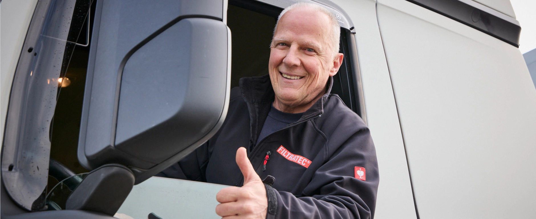 Mitarbeiter in FILTRATEC-Bekleidung sitzt im Führerhaus eines Lkw und zeigt lächelnd den Daumen nach oben.